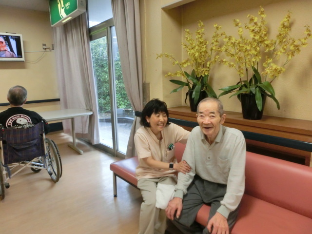 介護施設のラウンジで入居者と職員が笑顔で談話している風景